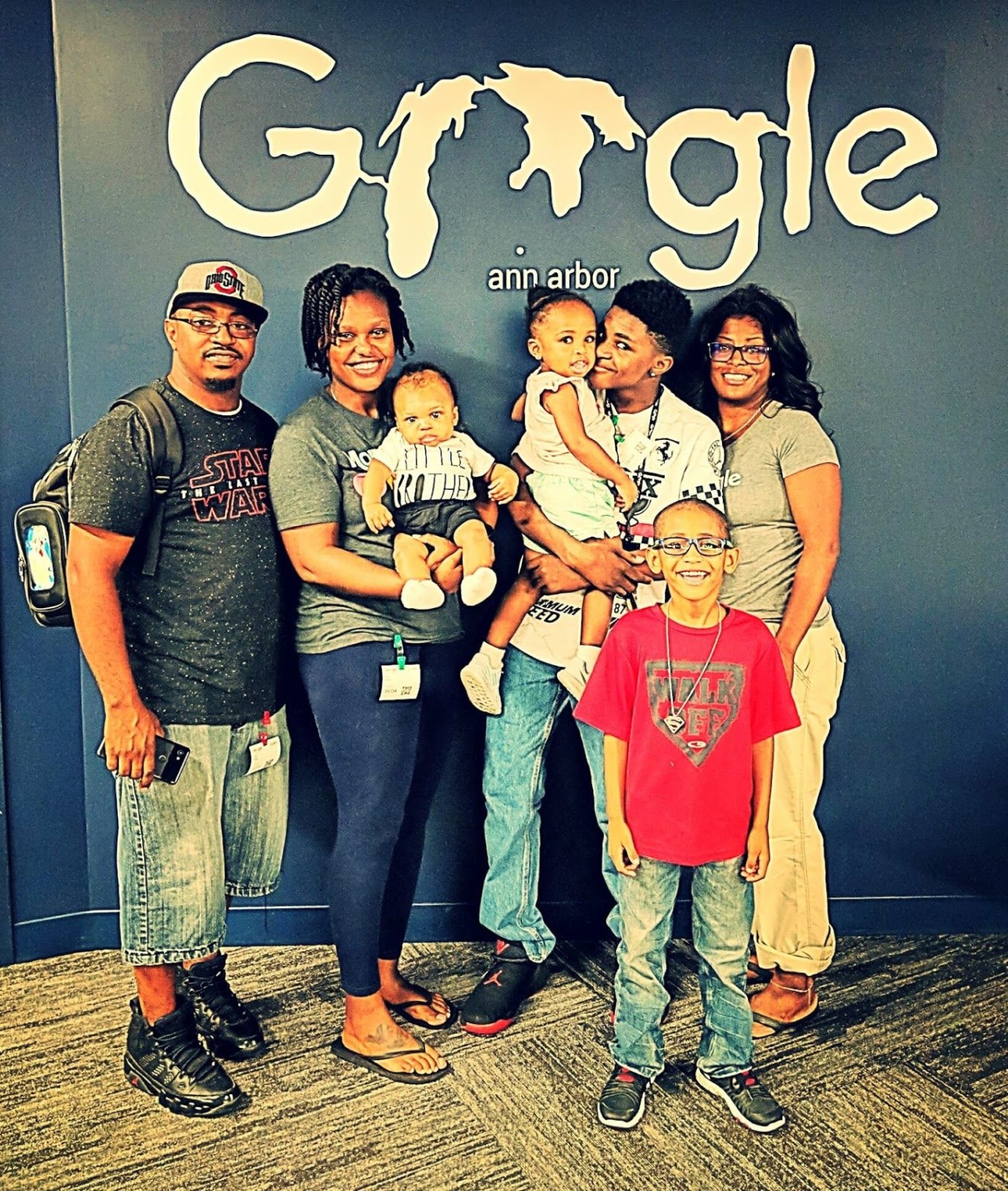 A smiling group of three adults and four children pose for a photo in front of a large Google sign that reads “ann arbor.”