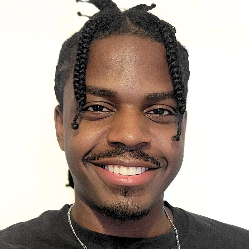 Headshot of a smiling young man with braided hair.