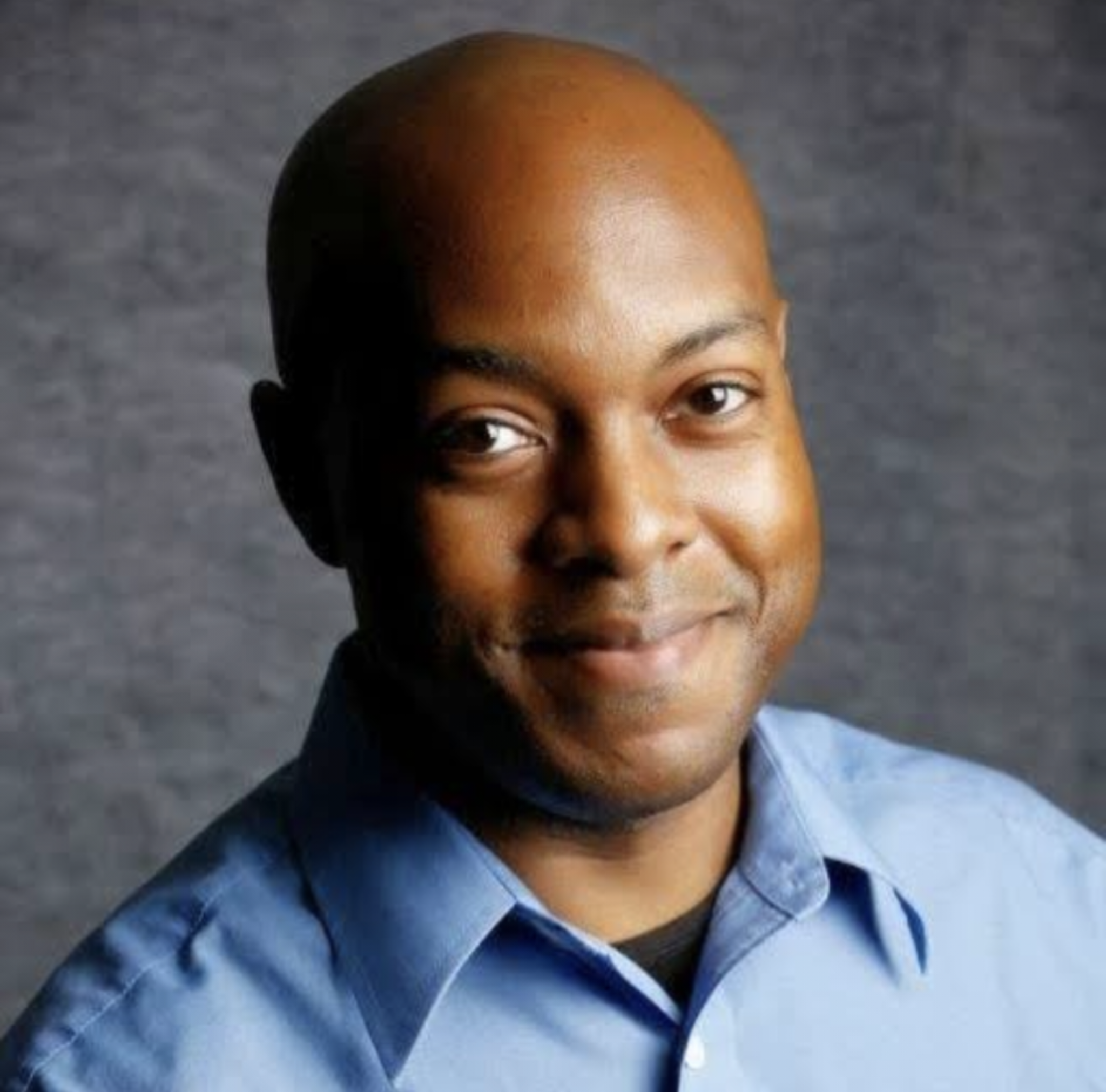 Head-and-shoulders portrait of a smiling Travis McCullough in a collared shirt against a neutral backdrop.
