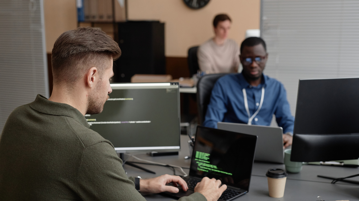 Young professionals working at laptops in a shared office, focused on coding on their screens.
