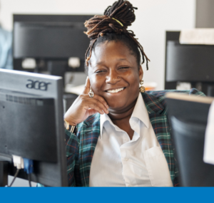 Smiling adult learner seated at a computer in a classroom, looking at the camera.