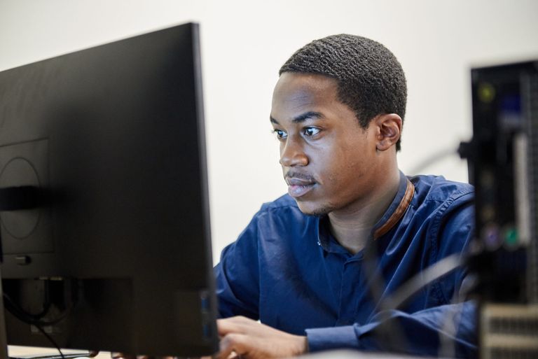 Young man focused on a computer screen, working at a desktop in a classroom.