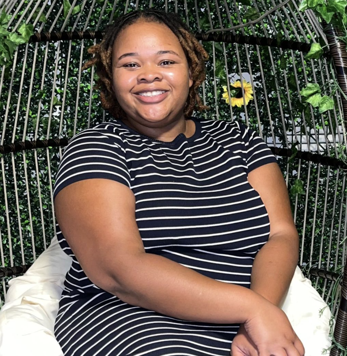Natasha Hurditt smiling, seated in a wicker pod chair with greenery behind her.