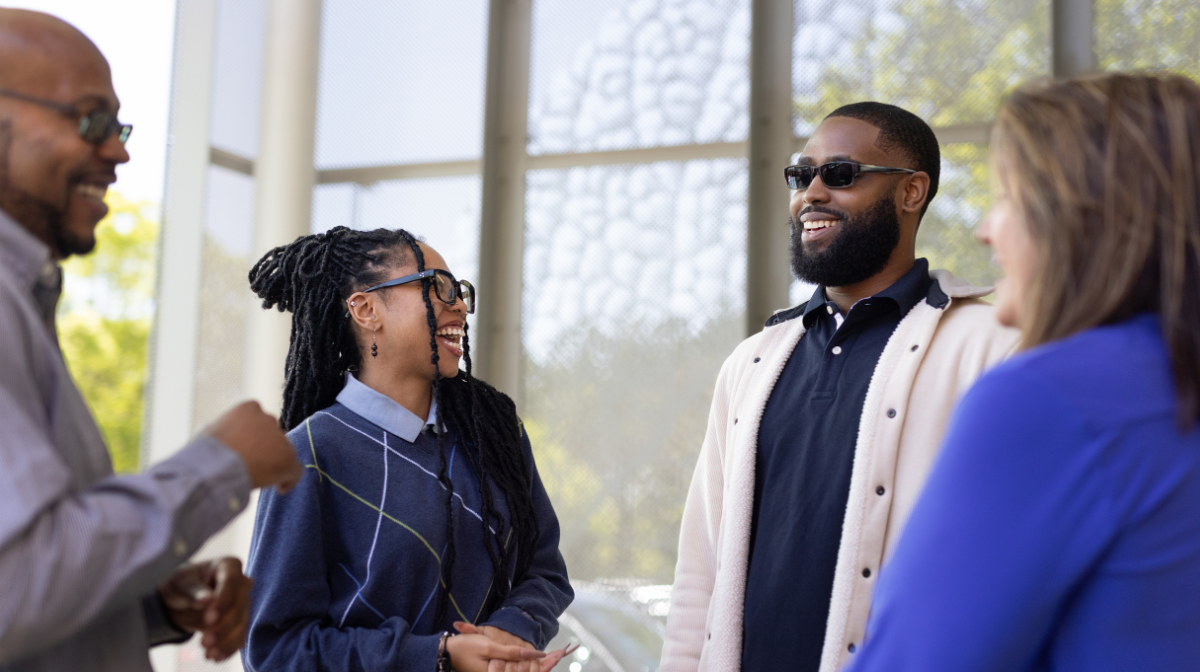 Four young professionals standing and smiling while conversing.