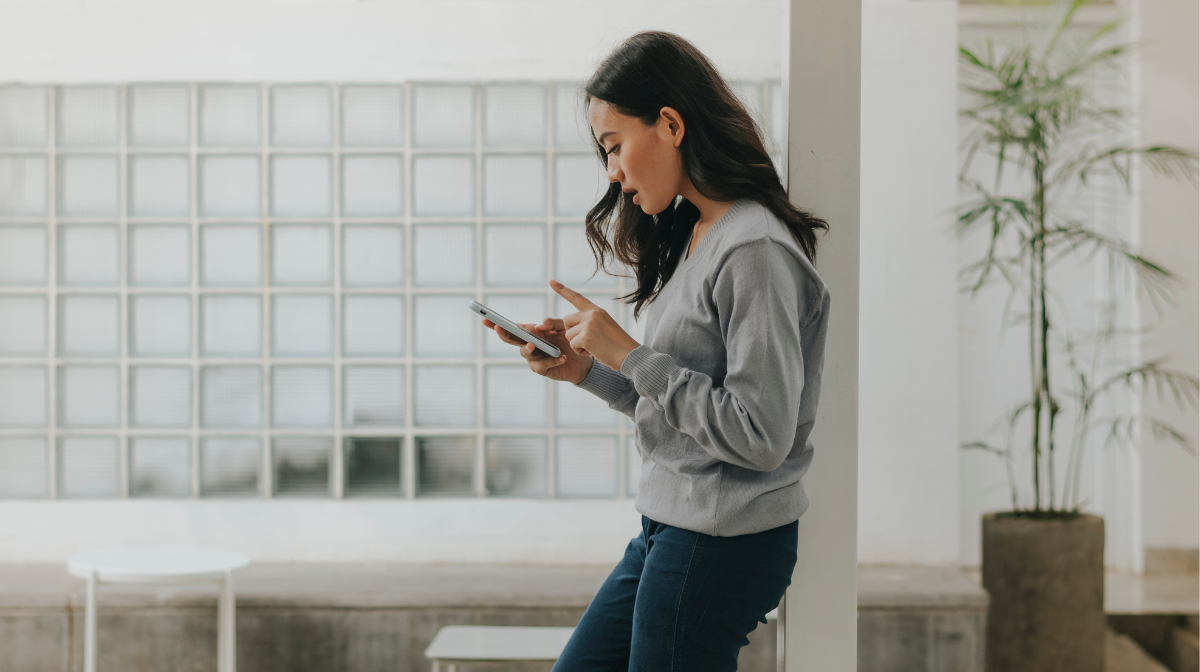 Young adult woman leaning against a pillar, using a smartphone.