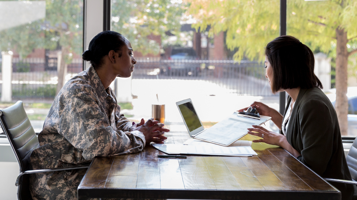 Female veteran in uniform meeting with a career counselor across a table, reviewing documents and a laptop.