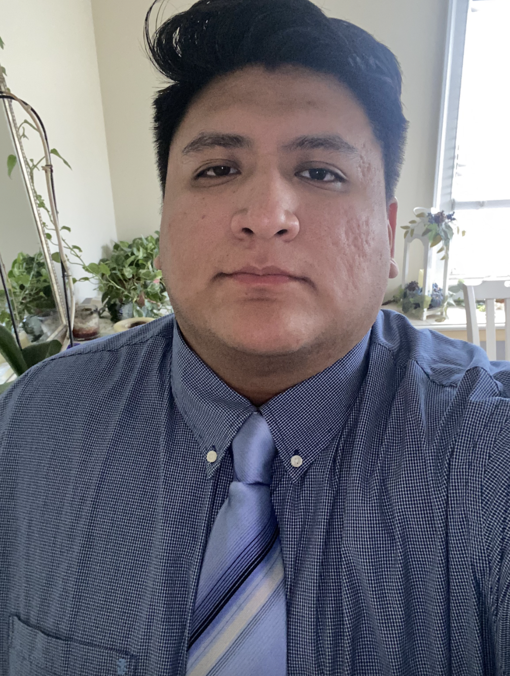 Young adult man wearing a button-down shirt and tie, looking straight at the camera.