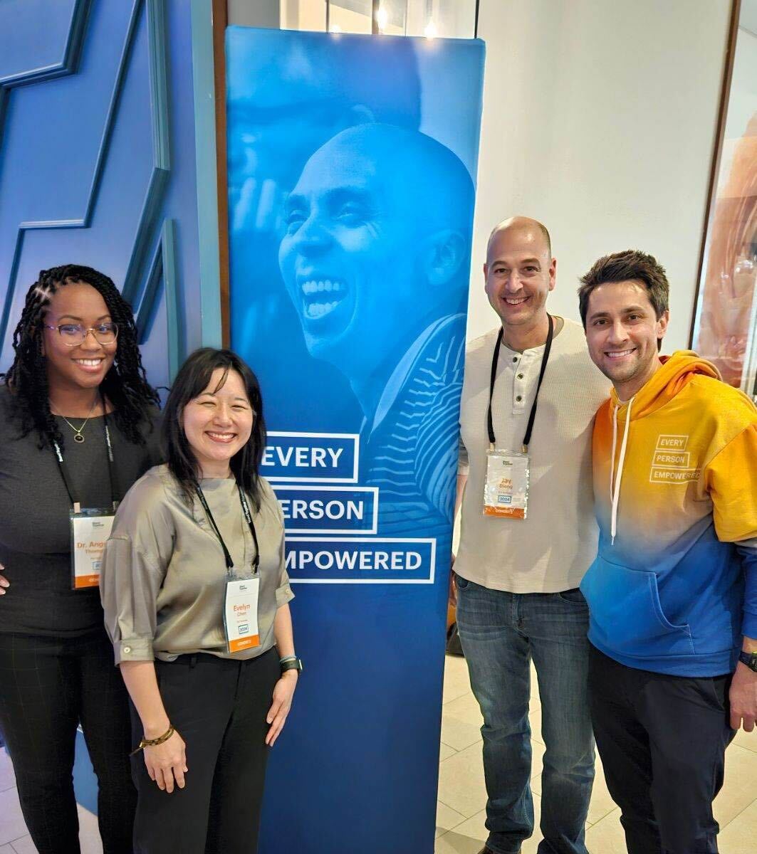 Four smiling adults wearing conference badges stand beside a tall blue banner that reads "Every person empowered."
