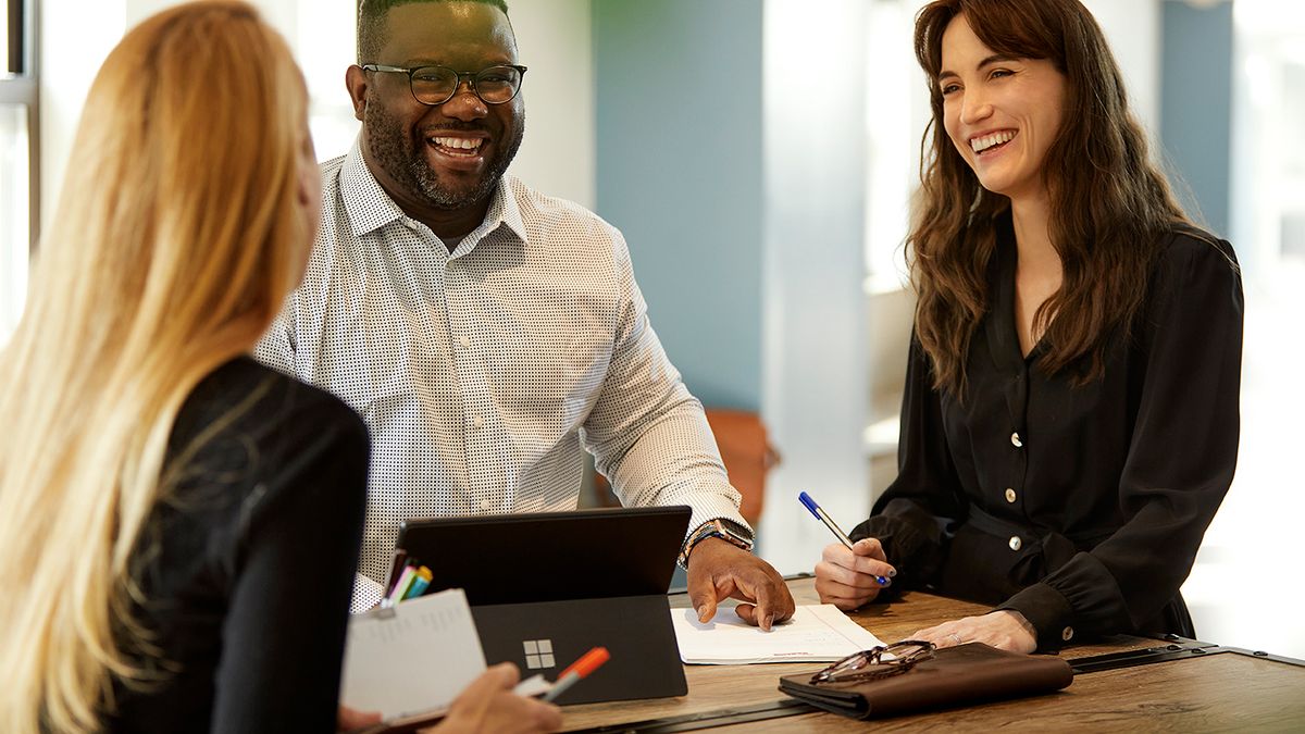 Three young professionals at a table smiling and in conversation during a collaborative meeting.