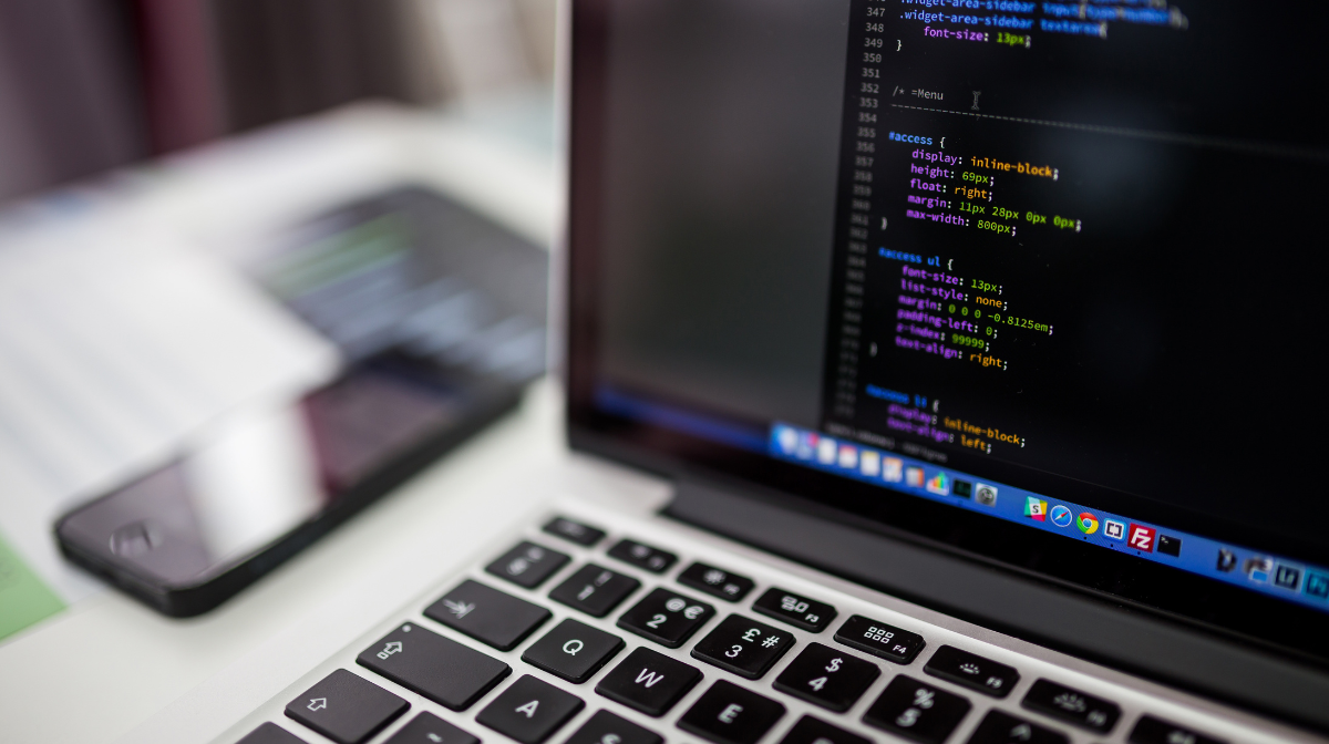Laptop screen showing lines of code beside a blurred phone on a desk.