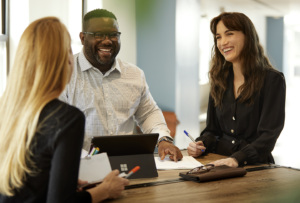 Three adult learners and an instructor sit at a table in a classroom, smiling and discussing together.