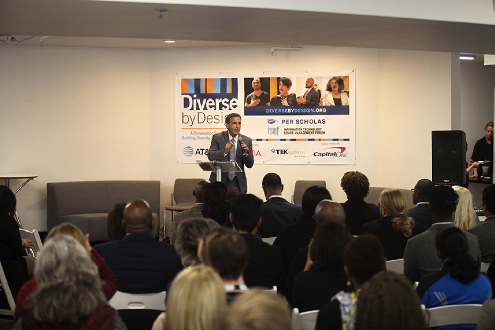 Man speaking at a podium to a seated audience in front of a "Diverse by Design" event banner.