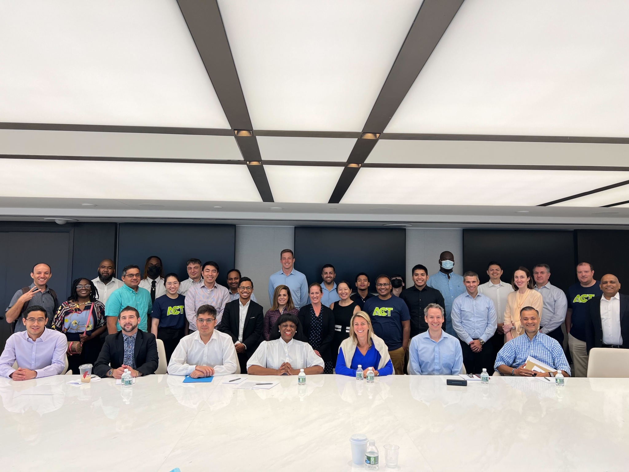 Group of adult learners and staff smiling in a conference room, seated and standing behind a long table.