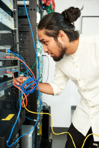 Young adult leaning into a server rack, connecting network cables to equipment.