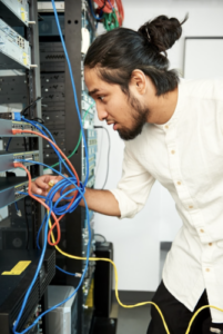 Young adult leaning into a server rack, connecting network cables to equipment.