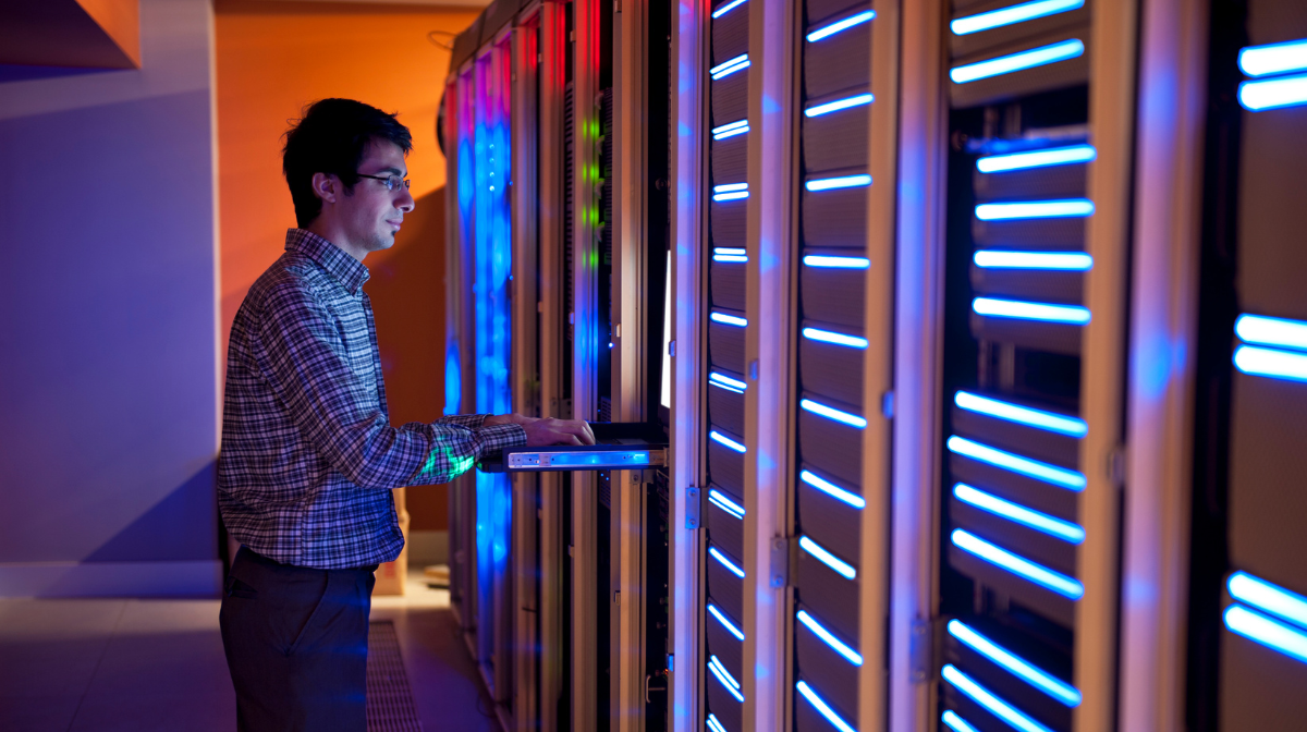 Young professional standing at a server rack using a slide-out keyboard to work on equipment in a data center.
