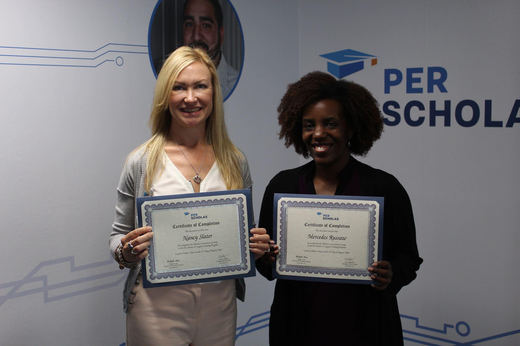 Two graduates holding Per Scholas certificates and smiling in front of a Per Scholas logo wall.