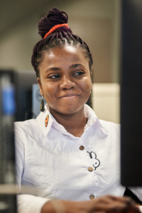 Woman smiling while working at a computer in a classroom or lab setting.