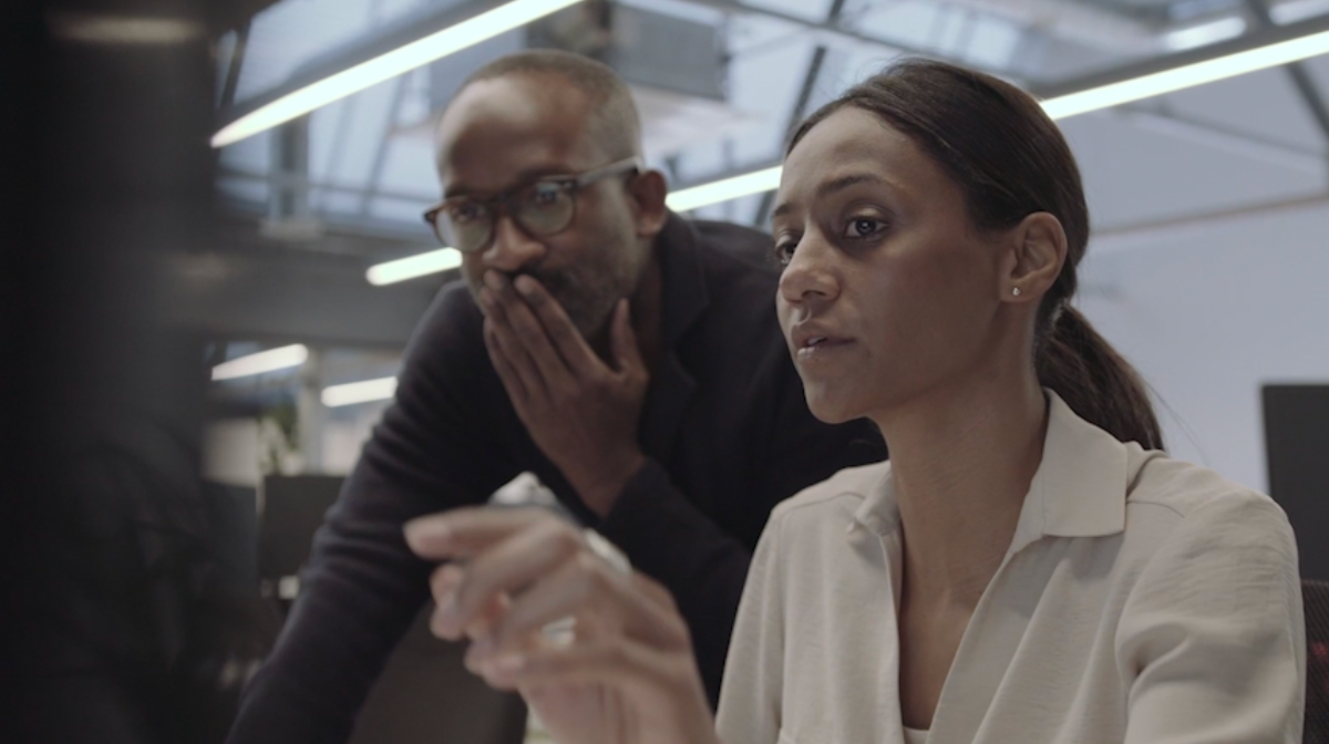 Two colleagues collaborate at a computer, the woman pointing at the screen while the man observes.