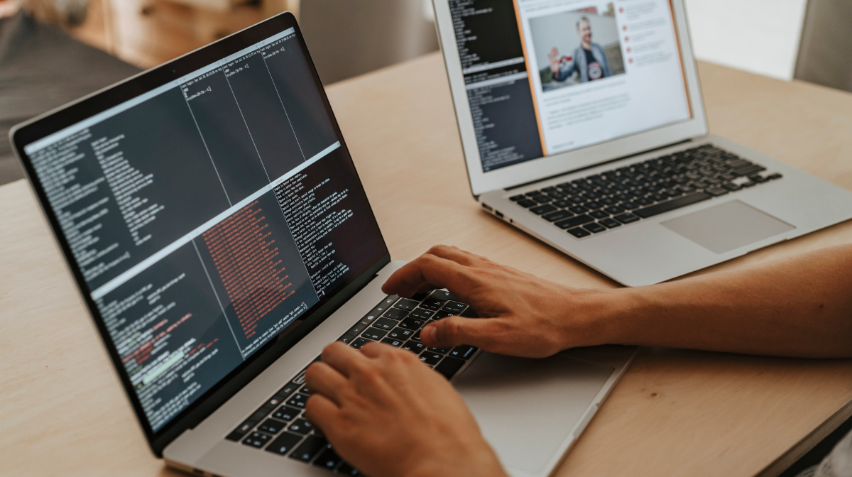 Person typing code on a laptop with another laptop showing a webpage.