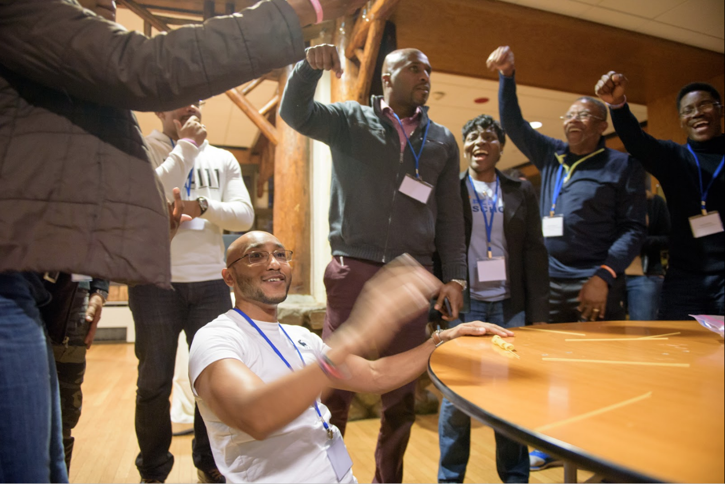 A group of adult learners smiling and cheering around a table while one person seated at the table.
