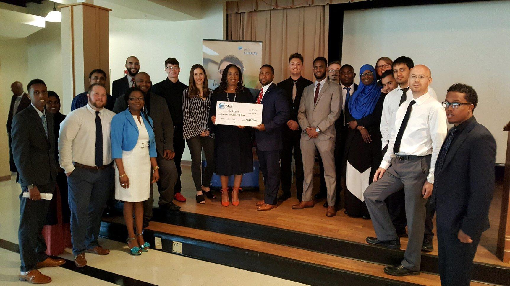 A diverse group of adults and staff standing on a stage holding an oversized check.