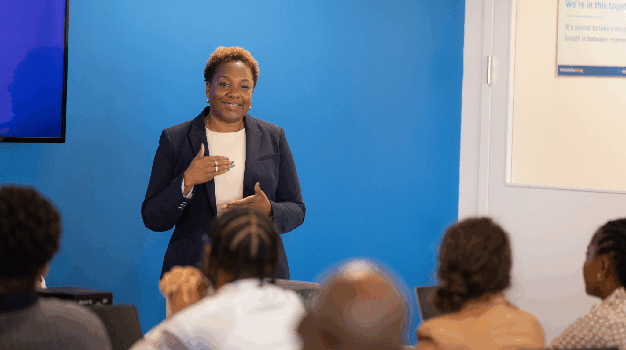 Instructor smiling and teaching a small learner classroom, speaking to seated students.