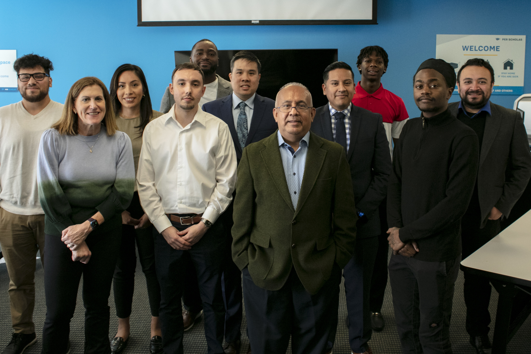 Diverse group of adult learners and staff standing together in a classroom, smiling toward the camera.