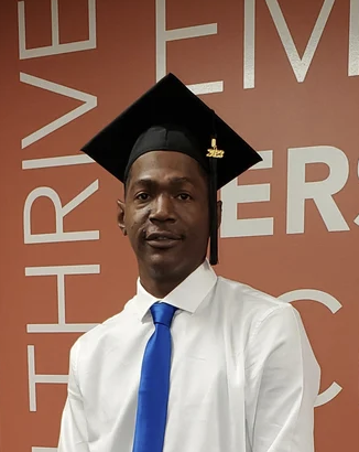 Young man in graduation cap and gown standing in front of a wall with large text that reads "THRIVE".