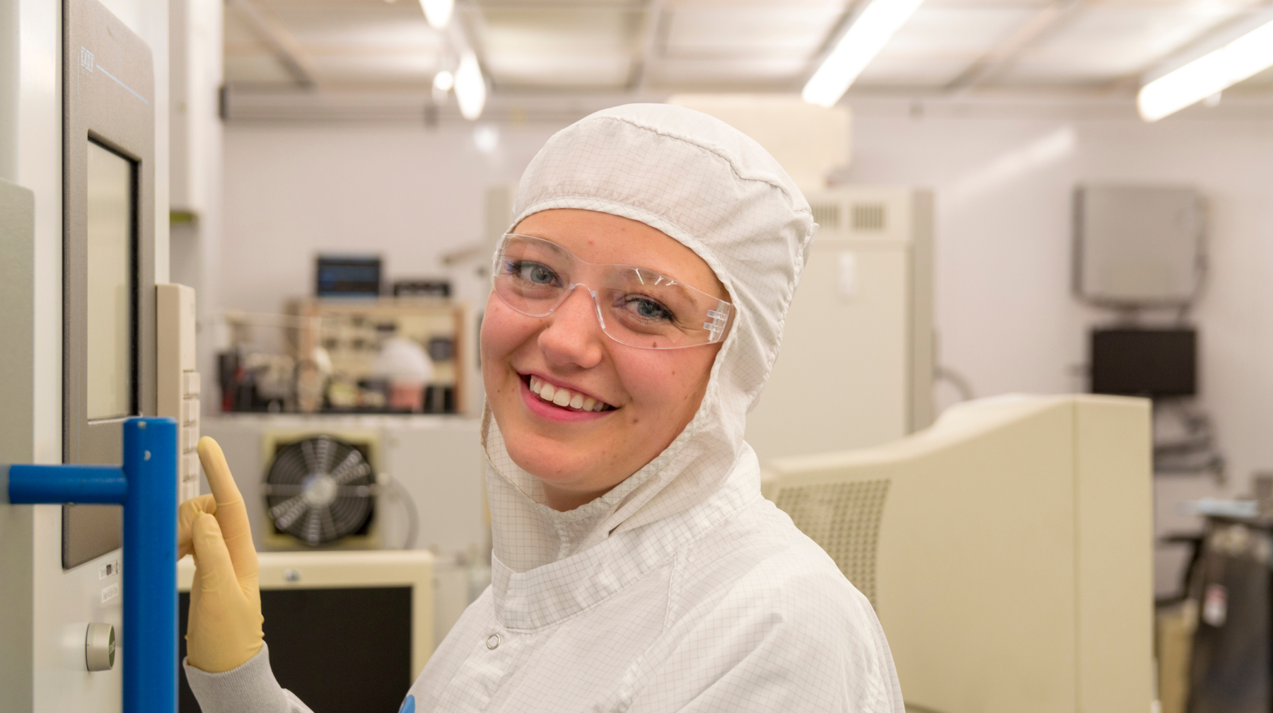 Smiling lab technician in cleanroom gear operating equipment in a lab.