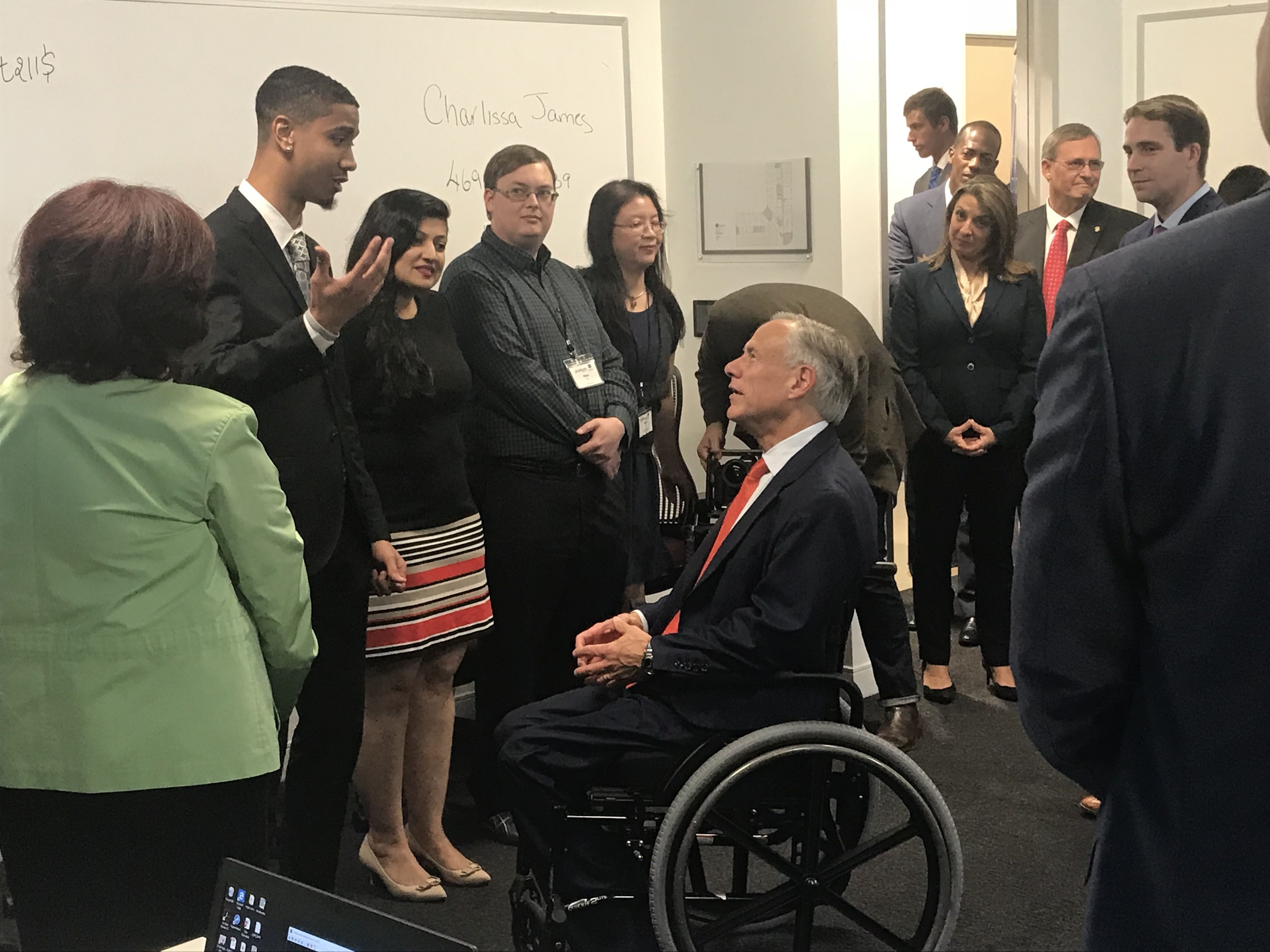 A group of adults in business attire listening to a man in a wheelchair speaking to them in an classroom setting.