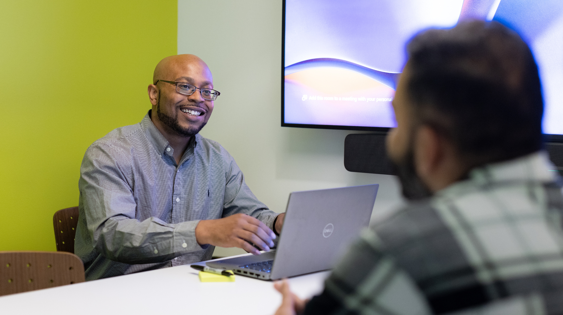 Two male learners having a friendly meeting at a table with a laptop and screen in a small conference room.