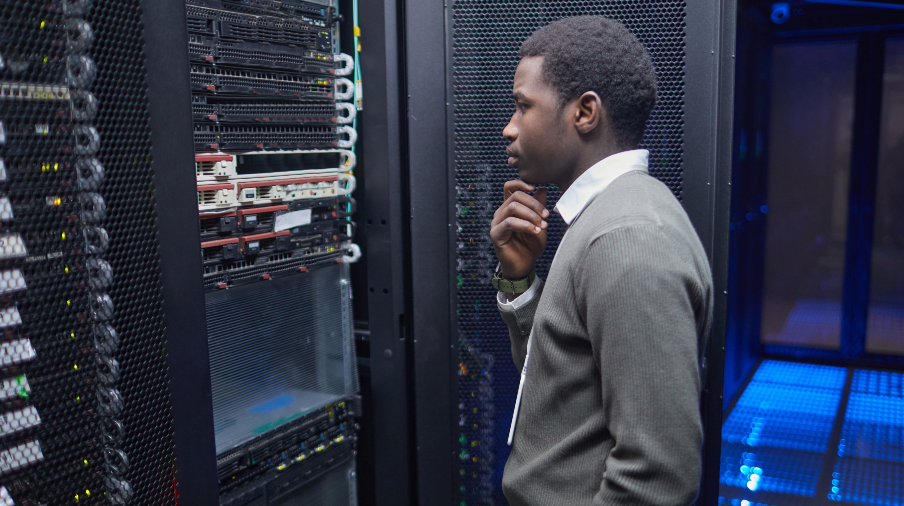 Man standing in a server room inspecting network equipment, appearing to troubleshoot or evaluate hardware.