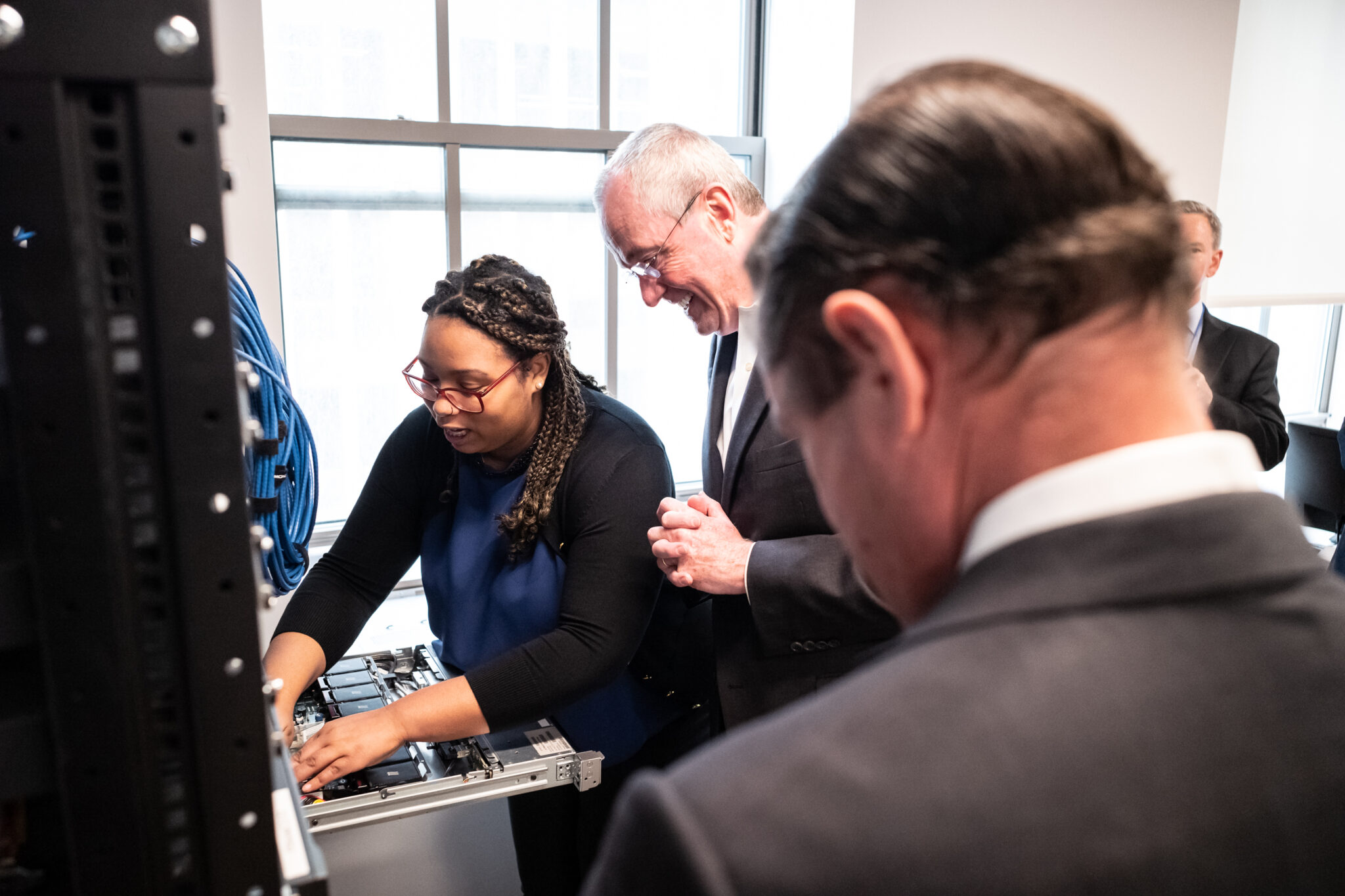 A young professional demonstrates server hardware inside a rack to other professionals.