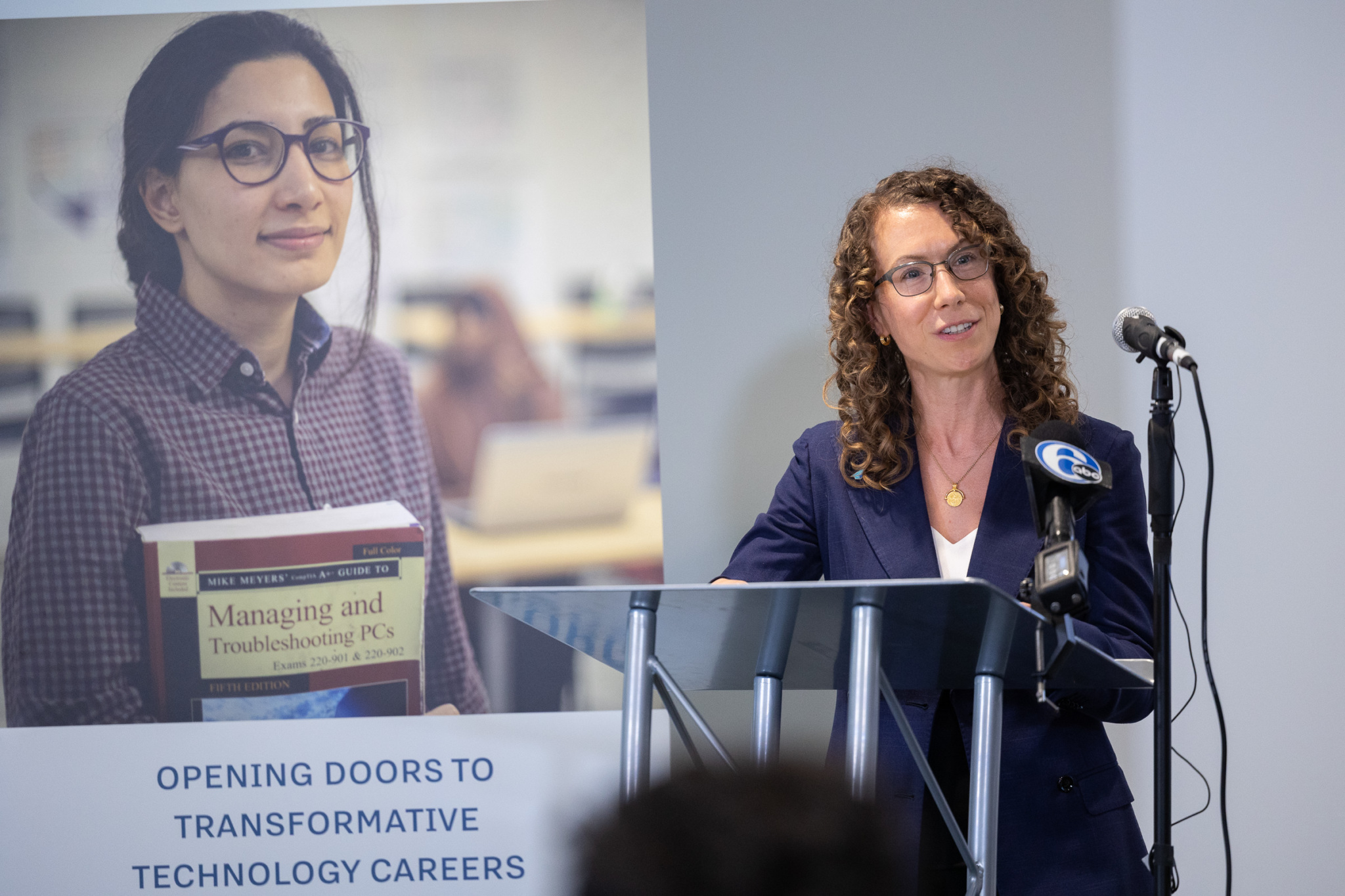 Woman speaking at a podium with a banner reading "Opening doors to transformative technology careers" next to her.