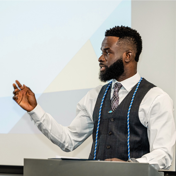 Akintunde Akinwande standing at a podium, gesturing with one hand.