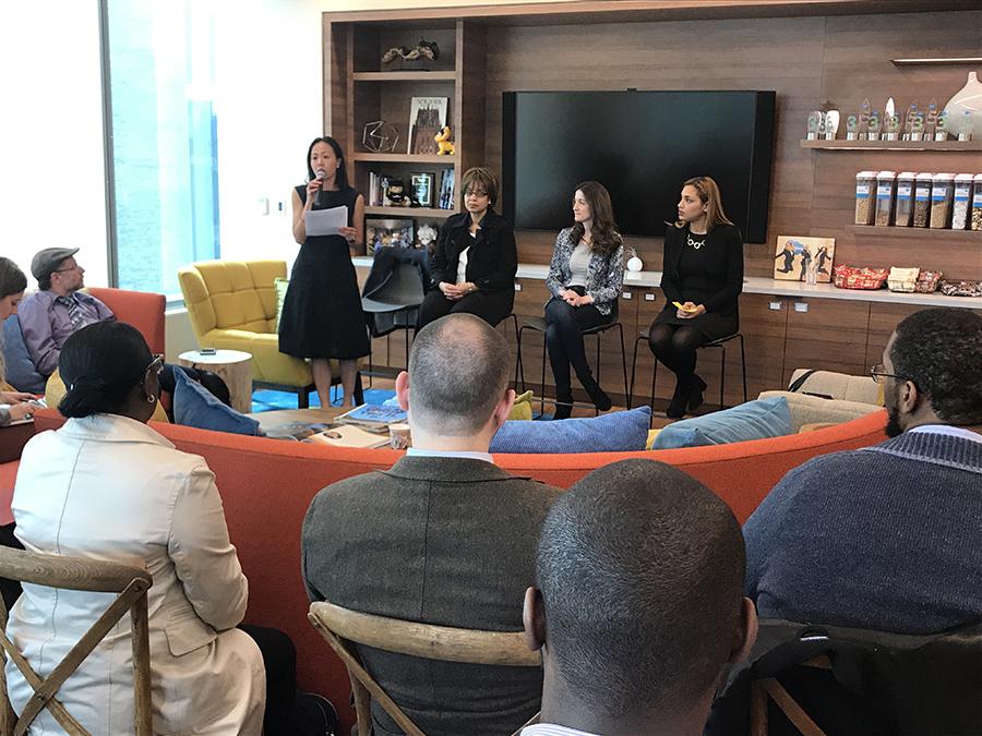 Woman speaking from a chair in front of a seated panel while an audience listens in an office space.