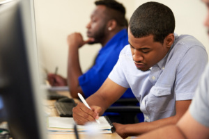 Adult learner concentrating at a desk writing notes in a classroom.