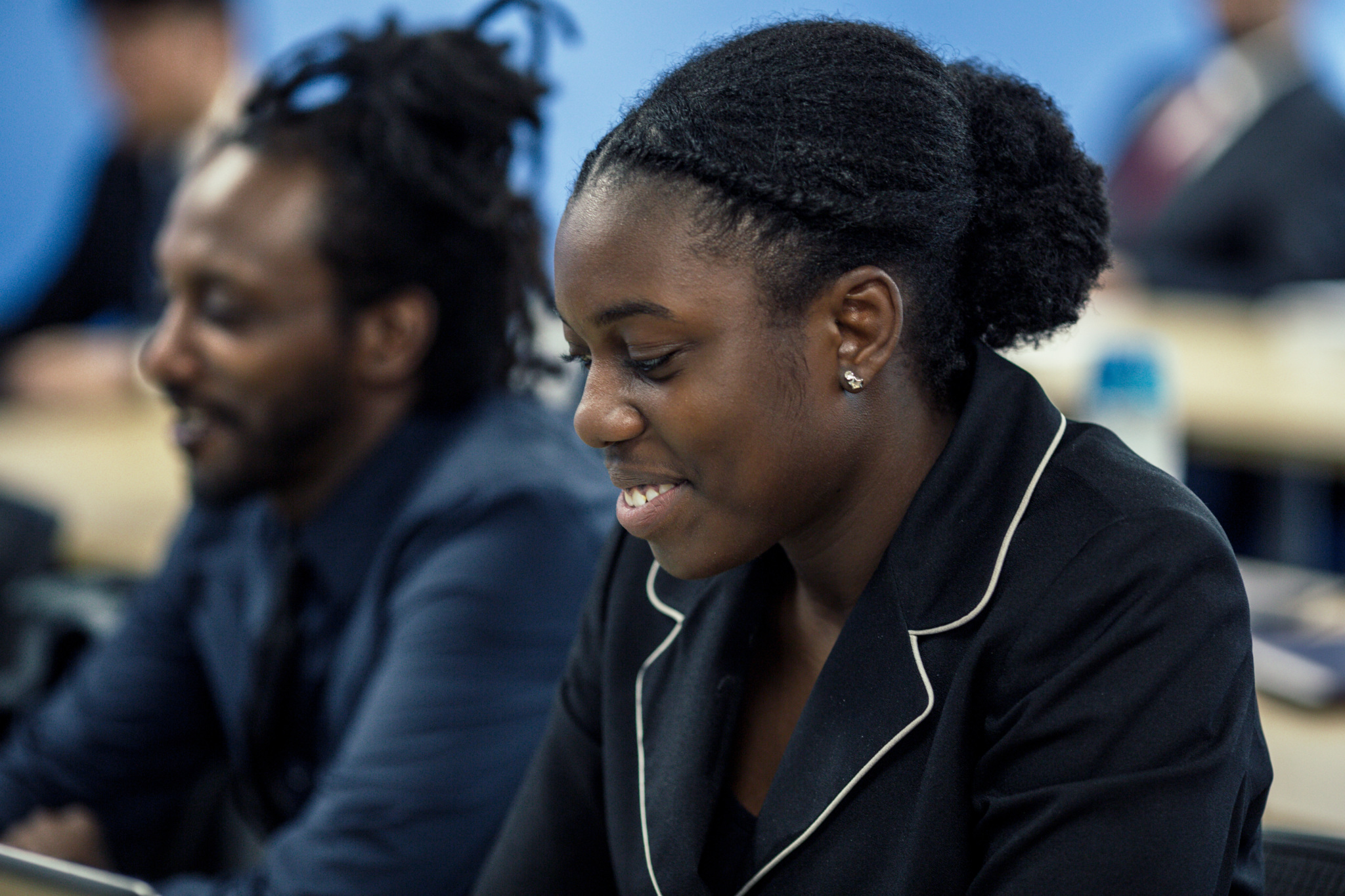 Young adult learner smiling and looking down while seated in a classroom.