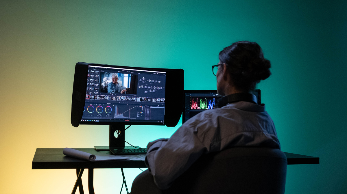 Person sitting at a desk editing video on dual monitors.