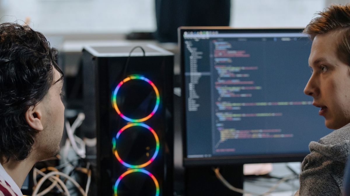 Two young male professionals collaborate at a desktop computer.