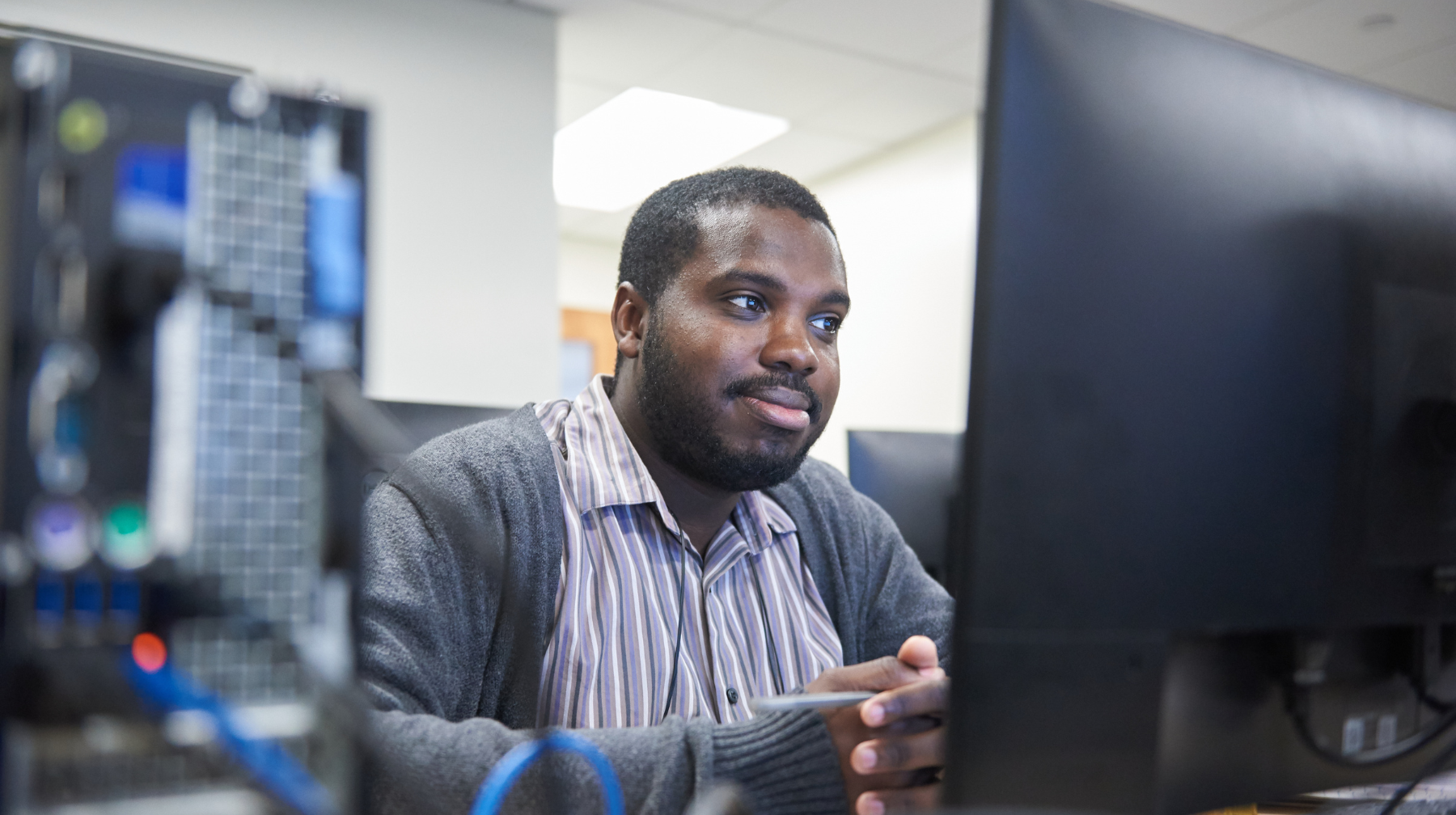 A man working attentively at a desktop computer in a tech lab.
