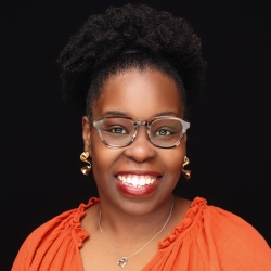 Headshot of a smiling woman wearing glasses and a necklace, looking directly at the camera.