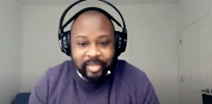Man wearing a headset speaking to a virtual audience in a home office.