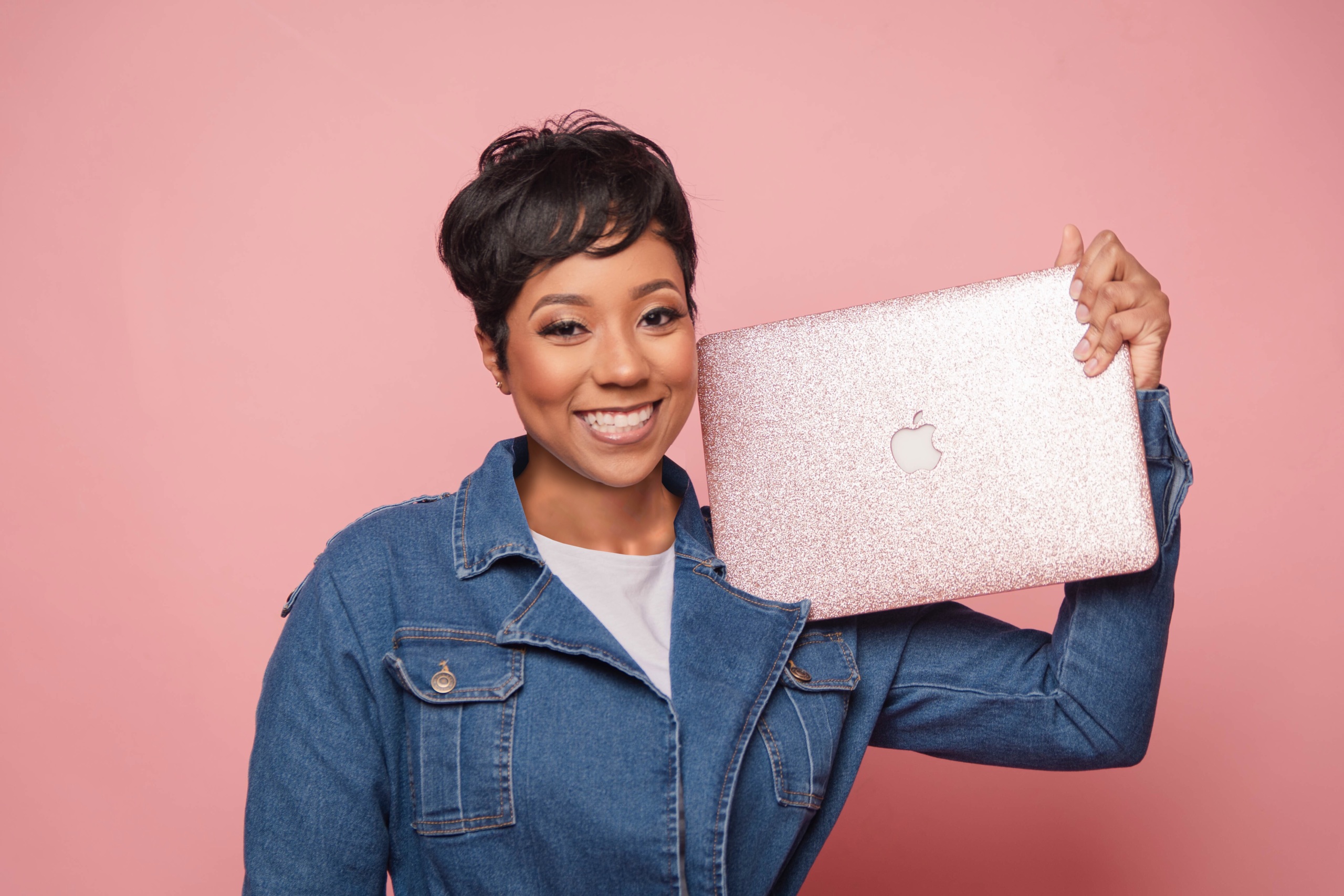 Smiling young woman holding a laptop beside her head.