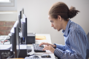 Young adult learner focused at a classroom computer, typing on a keyboard in a row of workstations.
