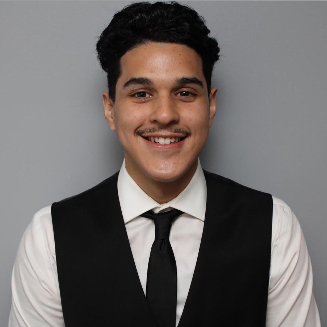 Young man smiling in a professional headshot wearing a shirt, tie, and vest.
