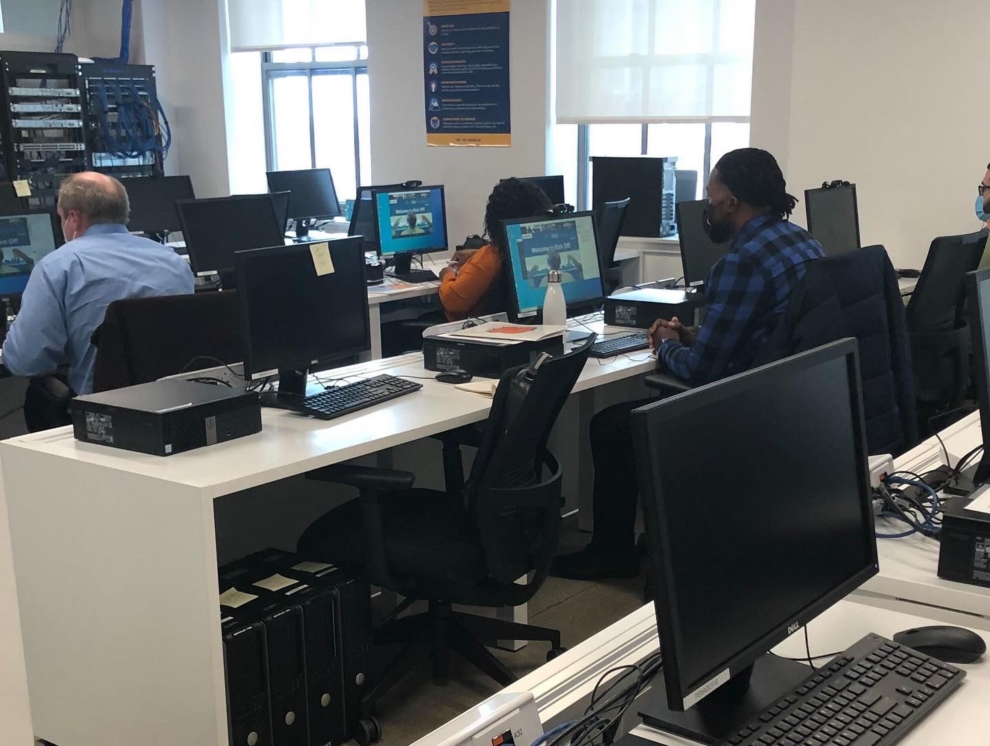 Adult students working at desktop computers in a classroom, facing monitors and learning quietly.