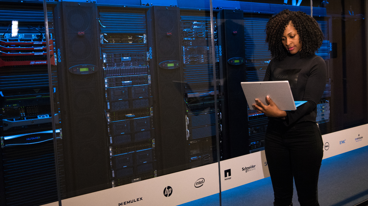 Woman standing in a server room holding a laptop.