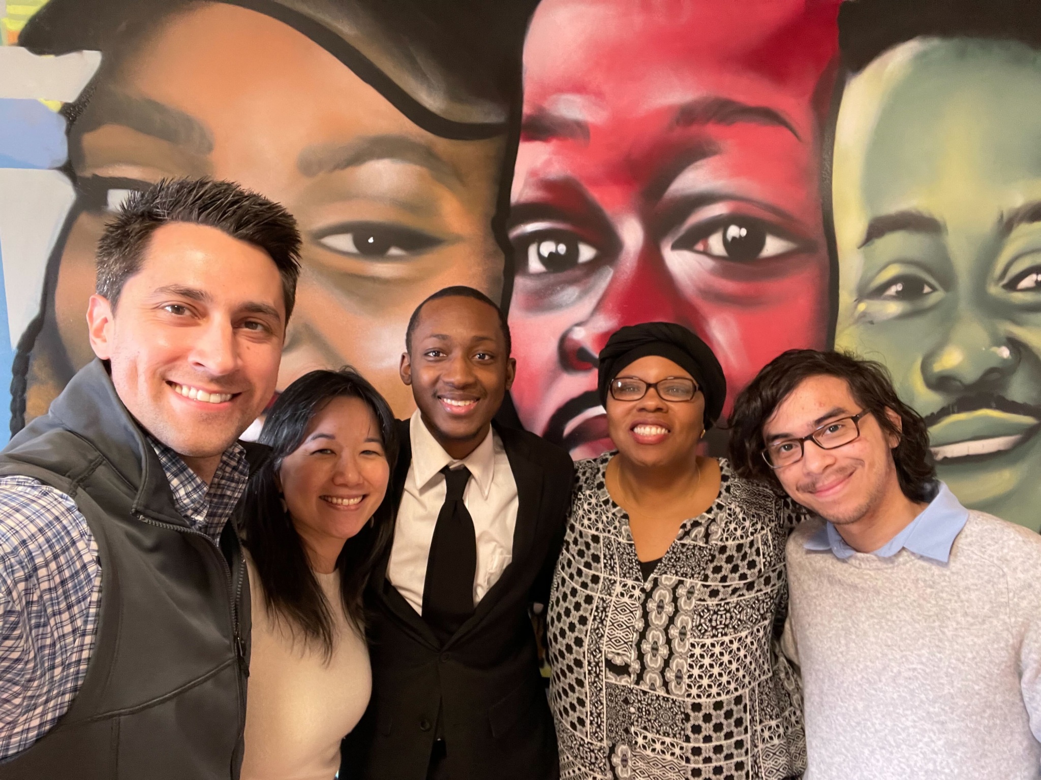 Five smiling adults together in front of a mural.